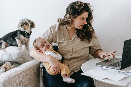A new mother holds her baby in one arm as she works on her laptop with the other.